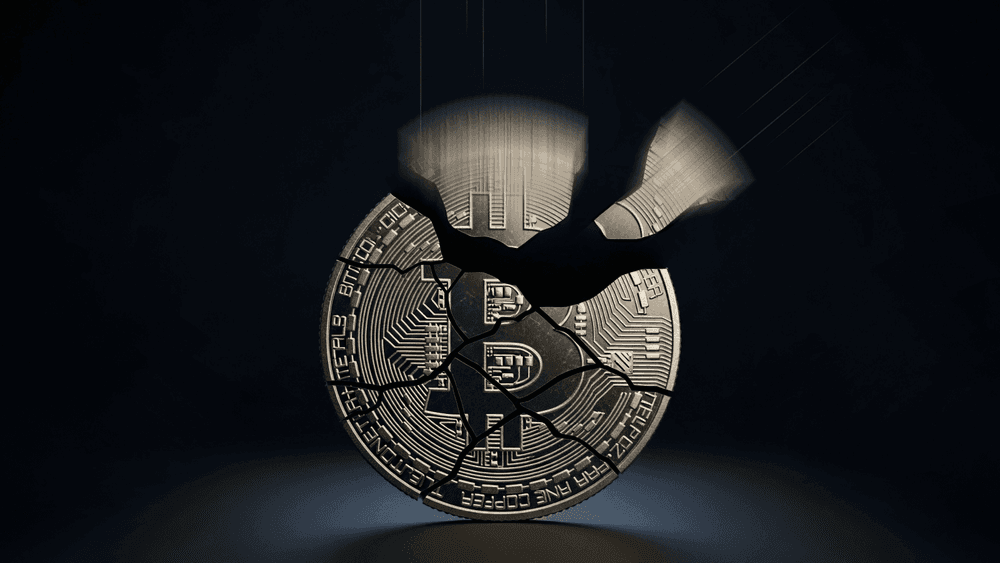 A cracked Bitcoin coin shattering into pieces against a dark background, symbolising a major Bitcoin price crash or market downturn.